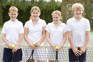 Four young friends with rackets on tennis court smiling