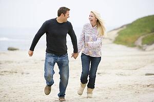 Couple running at beach holding hands smiling