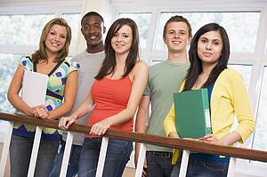 Five students in corridor leaning on railing with notebooks