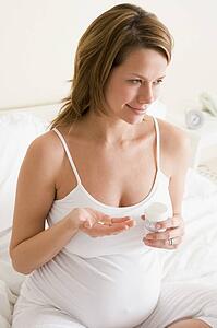 Pregnant woman in bedroom holding medicine and water smiling