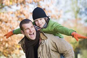 Father piggybacking son outdoors at park and smiling (selective focus)