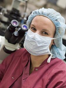 Embryologist sitting by microscope with mask on (selective focus)