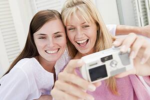 Two women on patio using digital camera smiling