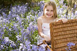 Young girl sitting outdoors with picnic basket smiling