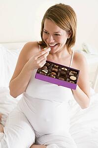 Pregnant woman in bed eating chocolate smiling