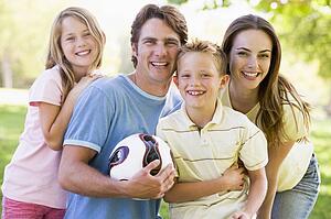 Family standing outdoors holding volleyball smiling
