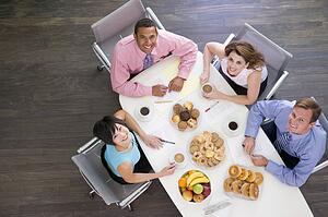 Four businesspeople at boardroom table with breakfast smiling