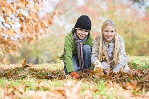 Two young children outdoors at park playing in leaves and smiling (selective focus)