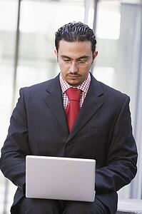 Businessman sitting outdoors by building with a laptop (high key/selective focus)