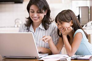 Woman and young girl in kitchen with laptop and paperwork smiling