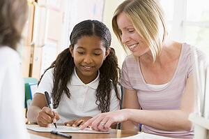 Student in class taking notes with teacher helping