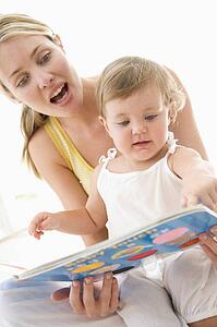 Mother and baby reading book indoors and pointing