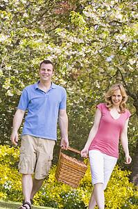 Couple walking outdoors with picnic basket smiling