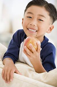 Young boy eating apple in living room smiling