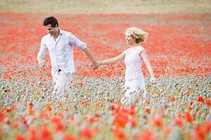 Couple walking in poppy field holding hands smiling