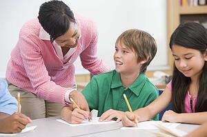 Students in class writing with teacher helping