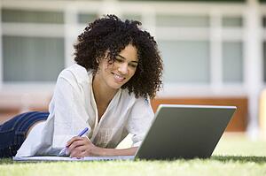 Woman lying on lawn of school with laptop