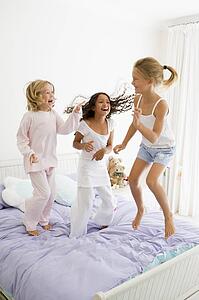 Three Young Girls Jumping On A Bed In Their Pajamas
