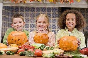 Three young friends on Halloween with jack o lanterns and food smiling