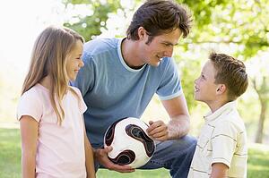 Man and two young children outdoors holding volleyball and smiling