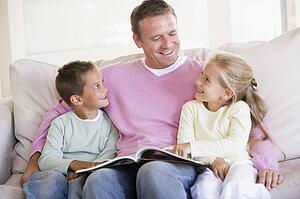 Man and two children sitting in living room reading book and smiling