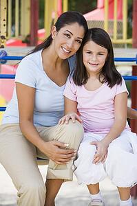Mother and daughter girl sitting on playground structure smiling (selective focus)