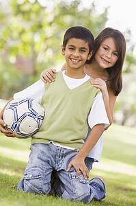 Two young children outdoors in park with ball smiling (selective focus)