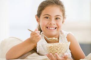 Young girl eating cereal in living room smiling