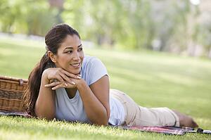 Woman lying outdoors at park with picnic basket smiling (selective focus)