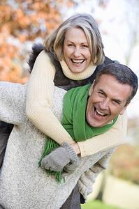 Senior man outdoors piggybacking woman and smiling (selective focus)