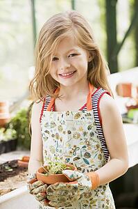 Young girl in greenhouse holding potted plant smiling