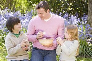 Father and two young children on Easter looking for eggs outdoors smiling