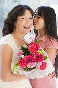 Granddaughter kissing grandmother on cheek holding flowers and smiling