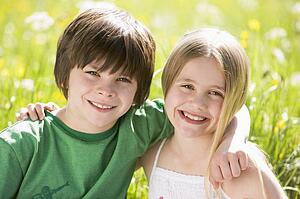 Two young children sitting outdoors arm in arm smiling
