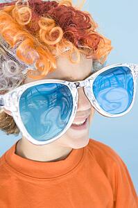 Young boy wearing clown wig and sunglasses smiling