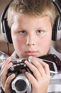 Young boy wearing headphones in bedroom holding many electronic devices