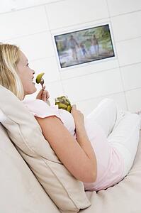 Pregnant woman watching television and eating pickles smiling