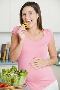 Pregnant woman in kitchen making a salad and smiling