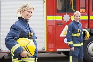 Firewomen standing by fire engine with another firewoman in background (selective focus)