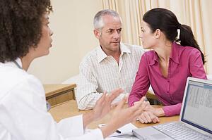 Doctor with laptop and couple in doctor's office frowning