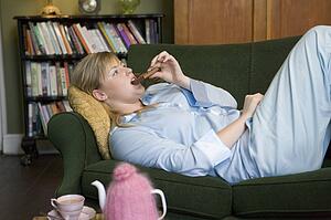 Young woman lying on sofa at home eating chocolate