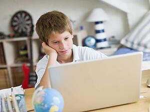 Young Boy Using A Laptop In His Bedroom