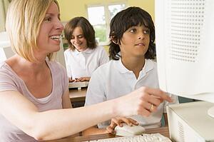 Student and teacher at computer terminal with student in background (selective focus)