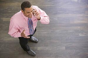 Businessman standing indoors using cellular phone smiling