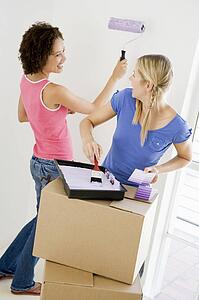 Two women painting room in new home smiling