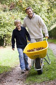 Father and son pushing wheelbarrow on path