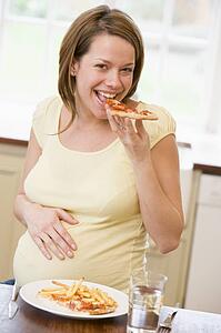 Pregnant woman in kitchen eating French fries and pizza smiling