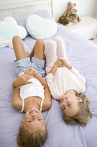 Two Young Girls In Their Pajamas Lying On A Bed