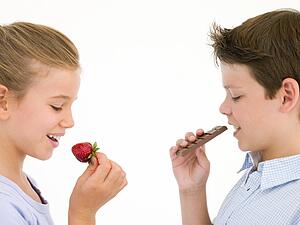Sister eating strawberry by brother eating chocolate bar