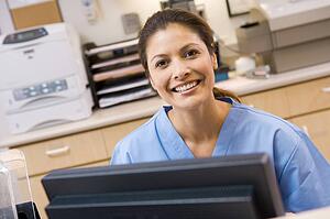 A Nurse Sitting At A Computer At The Reception Area Of A Hospital
